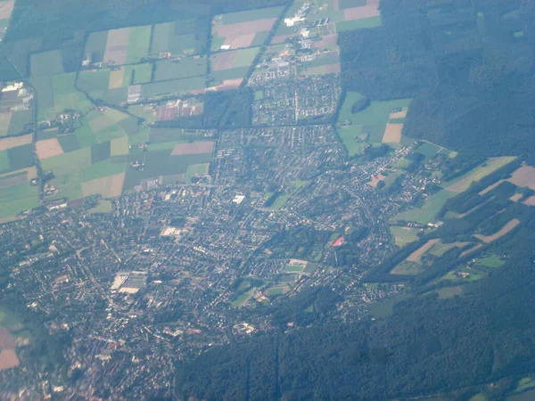 View from the plane of a big city, forests and cultivated fields near it. Blurred clarity from the height. Natural environment