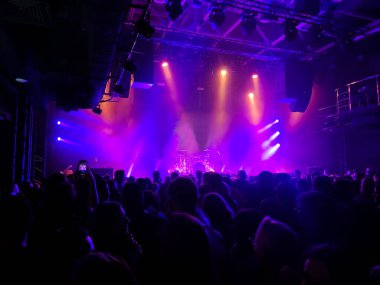 Konser salonunun sahnesi parlak renkli ışıklandırmayla doludur. Tanımlanamayan kişiler. Arka görünüm