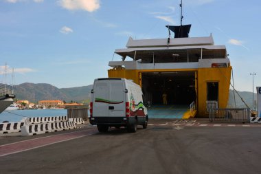 Limanda büyük bir feribot demirli ve bir nakliye aracı açık bir rampaya yanaşıyor. Ticari ve kargo taşımacılığı