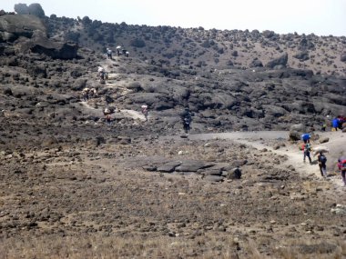 Turistler ve hamallar dolambaçlı bir kaya yolu boyunca dağa tırmanırlar. Bakış açısına göre görünüm