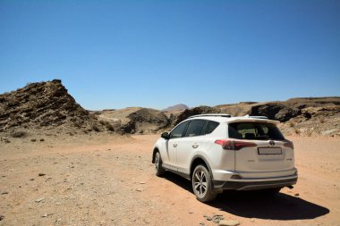 Tepelerin arasındaki kavurucu güneşin altında sırtı çöl yolunda duran beyaz bir araba. Turist konuları ve seyahatler