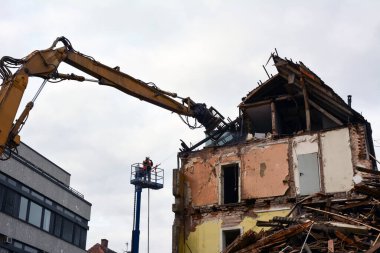 An excavator dismantles the ruins of an earthquake-damaged residential building with broken walls, windows and brick fragments