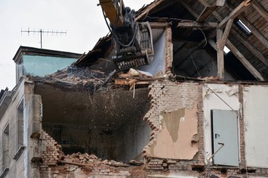 A residential building destroyed by an earthquake. An excavator with a bucket dismantles the floors to remove rubble