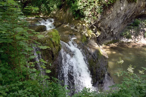 stock image A small river waterfall near a rock in a summer park. Natural background of the surrounding environment