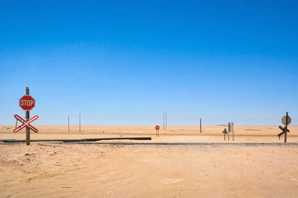 stock image View of railroad tracks and road signs in the desert. Behind are poles with electricity wires. The sky is clear and blue. Arid and hot climate