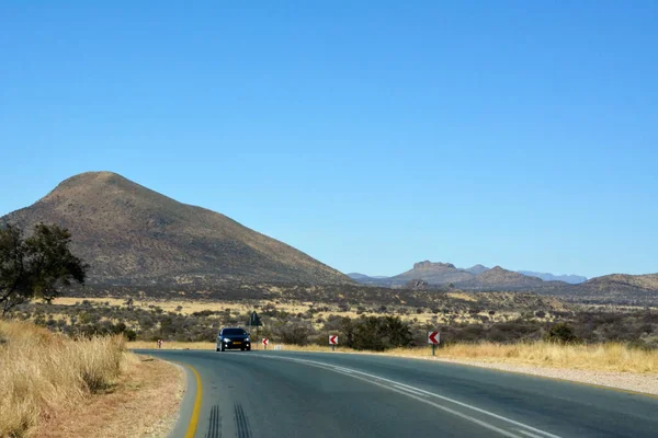 在沙漠中一条长长的柏油路 在蓝天的映衬下遥不可及 一辆汽车沿着公路在远处行驶 背景中的山脉 — 图库照片