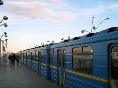 Yer istasyonundaki elektrikli metro treninin arabaları gökyüzünün arka planına göre perspektiftir. Tanımlanamayan yolcular yolda yürüyorlar.