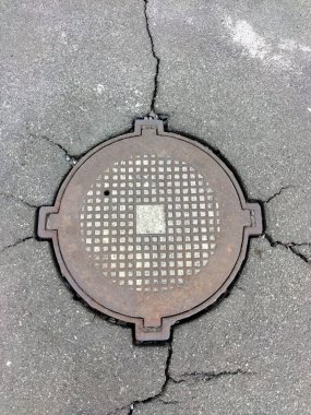 Eski asfalt bir yolda kapalı bir kanalizasyon kapağı çatlakların her yöne yayıldığı. Üst görünüm