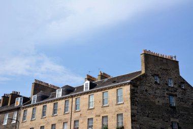 Pencereleri ve tuğla duvarları olan eski bir evin çatısı. Çatıda, mavi gökyüzünün arka planında, baca borularının ısınma sıraları var..