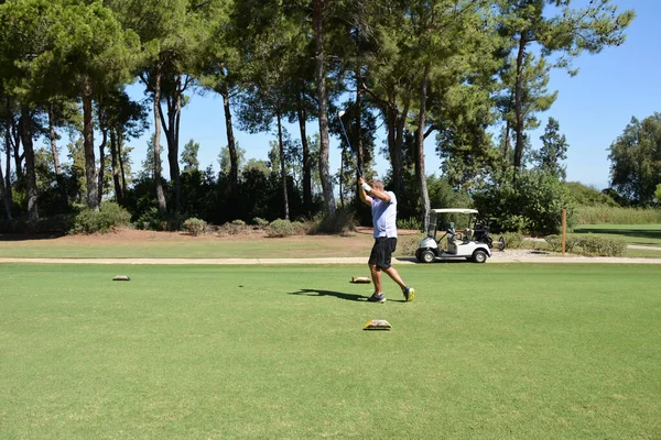 プライベートゴルフクラブの緑のクラブでゴルフボールを打つ男 背景にあるゴルフカートと木 アクティブな夏の豪華な休暇 — ストック写真
