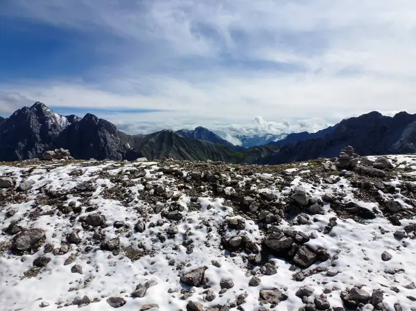 雪山に散らばった石の石の石の石灰岩は 遠くの明るい雲や他の山を持つ青空の背景に対してピークを迎えます — ストック写真