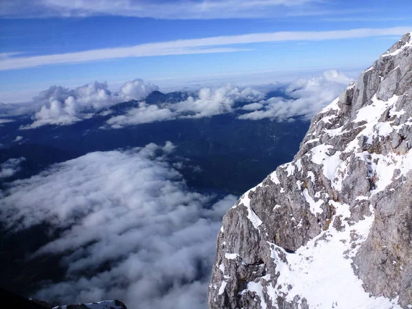 雪に覆われた岩山の頂上を右に その下には雲 青い空 冬の風景がある — ストック写真