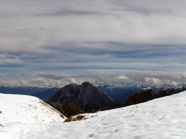 雪に覆われた山頂から近くの山への景色 その上には曇りの空がある 他の山の山の範囲は遠くにある — ストック写真