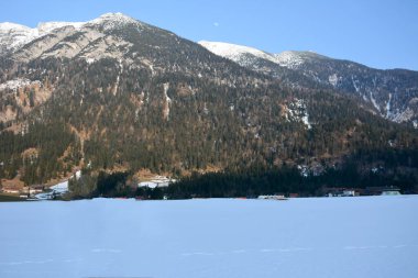 Ağaçlarla kaplı büyük kış dağları ve onların altındaki kayak merkezinin evleri. Kış manzarası