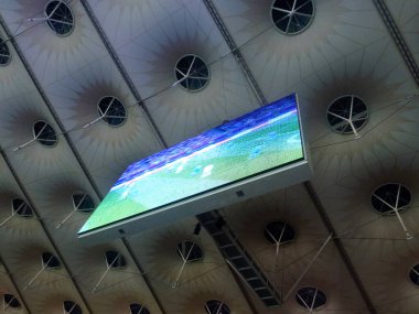 Büyük bir futbol stadyumunun çatısının altında ekranı olan bir skor tabelası. Aşağıdan görüntüle