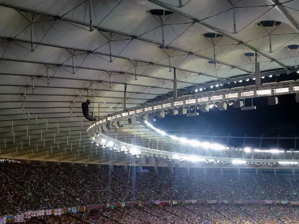 Brightly lit roof of a large football stadium with a hole in the middle. View from below