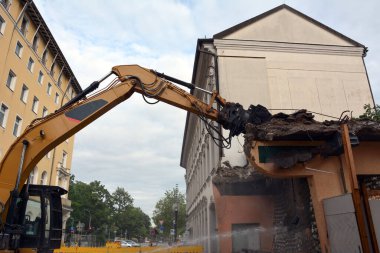 Manipülatör vinçli bir kazıcı kullanarak eski bir binanın duvarını yapanların sökmesi. Aşağıdan görüntüle