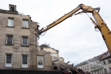 Manipülatör vinçli bir kazıcı kullanarak eski bir binanın duvarını yapanların sökmesi. Aşağıdan görüntüle