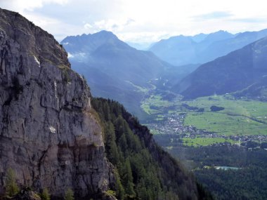Mavi ufku olan yüksek bir dağ. Ön planda, yamaç yeşil orman ve bulutlarla kaplıdır. Güzel doğal manzara