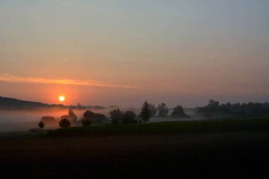 Güneşin açık bir gökyüzünde battığı akşam çayırlarının üzerinde bir sis süzülüyor.
