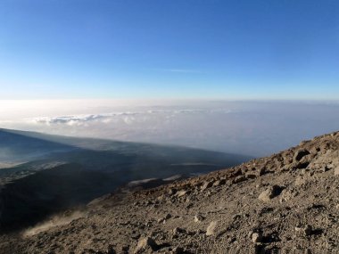 Dağdan, toprak ve taşlarla kaplı yamaçtan aşağıdaki manzaraya ve ufuktaki mavi gökyüzüne bak. Soğuk doğa manzarası