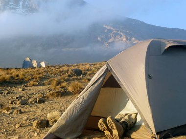 Yürüyüş botlarının içindeki ayaklar dağın tepesindeki çadırdan görülebilir. Aktif bir turist ve gezginin dağ yürüyüşünde olduğu sabah