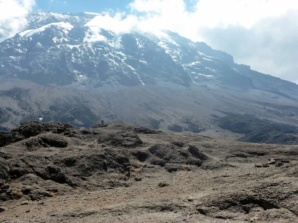 Parlak mavi bir gökyüzünde kayalık, karlı bir dağın manzarası. Güneşe karşı aşağıdan bak