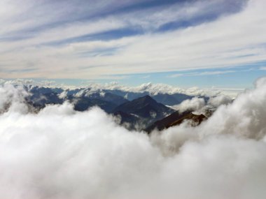 Beyaz bulutların arasından dağ tepelerine ve üzerlerindeki mavi gökyüzüne bak. Dağ doğal manzarası