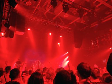 Parlak bir rock konseri sahnesi. Salonda bir sürü seyirci var. Salondan bak.