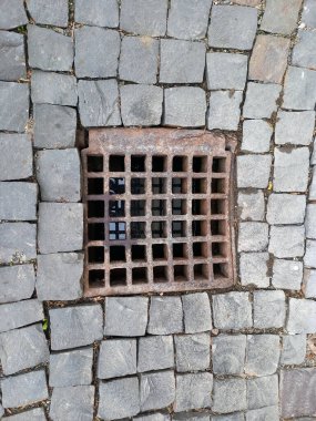 Taş kaldırımda paslı demir ızgaralı kanalizasyon.