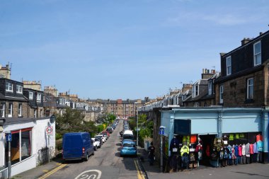 Kenarlarında arabalar ve sokak giyim mağazaları olan eski şehir caddesi.