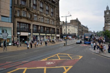 Tarihi bir İtalyan şehrindeki eski evler. Yanlarından turistler ve gençler geçiyor, şehir ulaşımı geçiyor.