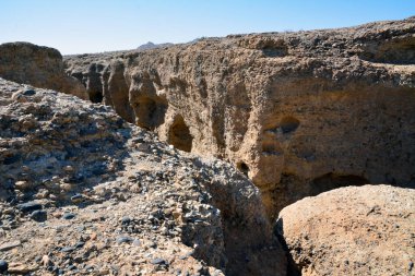 Mavi gökyüzünün altında parlak güneşin altında bir kabuğu olan derin kayalık bir kanyon. Çöl manzarası