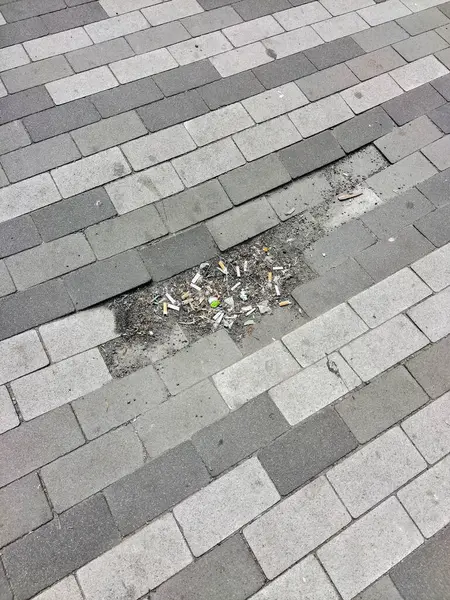 A worn-out street tile pavement with trash in a hole. Poorly constructed pavement surface. View from above.