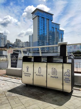 Uygun yazıtlara sahip ayrı çöp toplama için çelik kaplar modern gökdelenlerin arka planında fayanslı bir kaldırımda yer almaktadır.