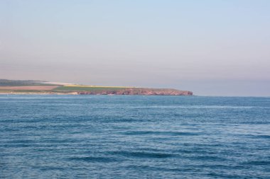 Sakin dalgalarla deniz manzarası ve üzerinde tarlalar ve açık gökyüzü olan uzak kıyılar. Doğal resimsel manzara.