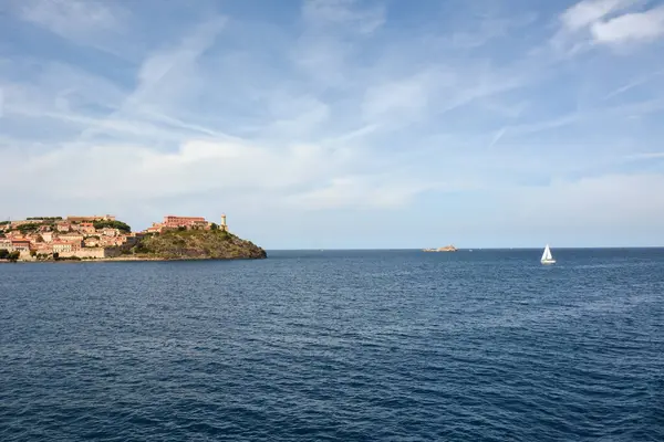 Seascape on the far shore with a lighthouse and ancient houses located on the hills. A yacht is sailing near the shore. Natural picturesque landscape