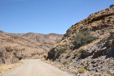 Çöldeki taştan tepeler arasında mavi gökyüzünün altında toprak bir yol. Vahşi doğada turizm ve eğlence.