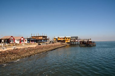 Parlak gün ışığında, deniz kıyısındaki katamaranlar, tekneler ve tekneler için binalarla dolu bir taş tükürüğe özel demirleme.