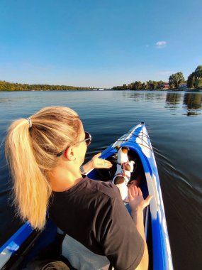 Genç sarışın bir kadın, Jack Russell teriyerinden bir köpekle geniş bir nehirde bir teknede yüzüyor. Doğada evcil hayvanlarla turizm ve eğlence.