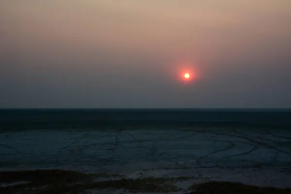 A distant dim sun sets in a clear sky over the evening desert. The surface of the desert is almost invisible.