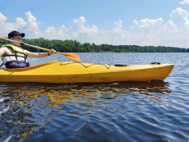 Geniş bir nehirde kayak yapan genç bir çocuk can yeleği giyiyor ve egzersiz yapıyor. Aktif spor hayatı ve eğlence