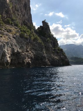 Deniz dalgalarının üstündeki gölde asılı duran kayalar. Üzerlerinde beyaz bulutlu parlak bir gökyüzü var. Doğal deniz turistik arazisi