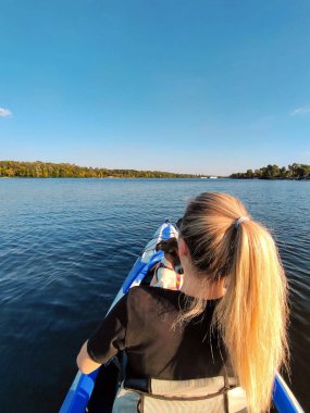 Genç sarışın bir kadın omzunda Jack Russell teriyer köpeği tutuyor. Geniş bir nehirde bir teknede yelken açıyorlar. Doğada evcil hayvanlarla turizm ve eğlence.