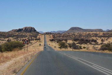 Açık mavi gökyüzünün altında çölde asfalt yol perspektifi. Yol uzak dağlara ve tepelere çıkar.
