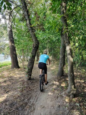 Parkta bisiklet süren genç bir kadın. Doğada aktif bir eğlence. Ağaçların arka planında arka görünüm