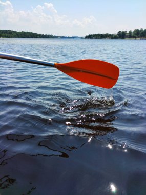 Teknenin küreği geniş nehrin ve mavi gökyüzünün arka planında kırmızıdır.