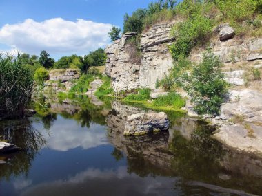 Eski taş ocağının kayalık yamaçları suyla doluydu ve bir göl oluştu. Çimen ve taşlar suya yansır. Güzel yerlerin doğal manzarası
