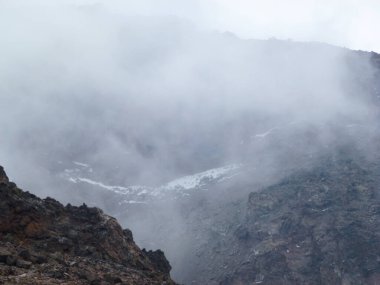 Dağın kayalık yamaçlarının beyaz sisle kaplı görüntüsü. Dağ turizmi manzarası