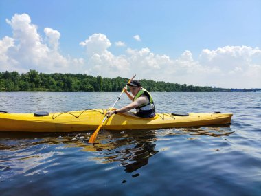 Genç bir beyaz adam nehrin arka planında ve uzak kıyılarda kano çalışması yapıyor. Spor ve aktif bir yaşam tarzı